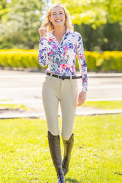 Full body front view of a female model wearing the Amethyst Watercolor Floral Kastel 1/4 Zip Long Sleeve Sun Shirt and tan breeches while walking outside on grass