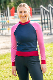 Front view of a female model wearing the navy, hot pink, and wine Kastel Crewneck Sweater with a jump arena in the background