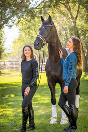 View of 2 female models wearing the Sailor Blue abd Black Kastel Crewneck Sweaters while standing outside in front of a black horse