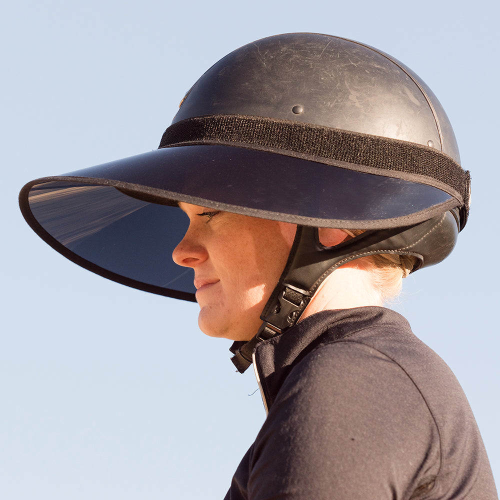Side view of a female model wearing the black EquiVisor VUE Sun Visor over a black helmet with a blue sky background