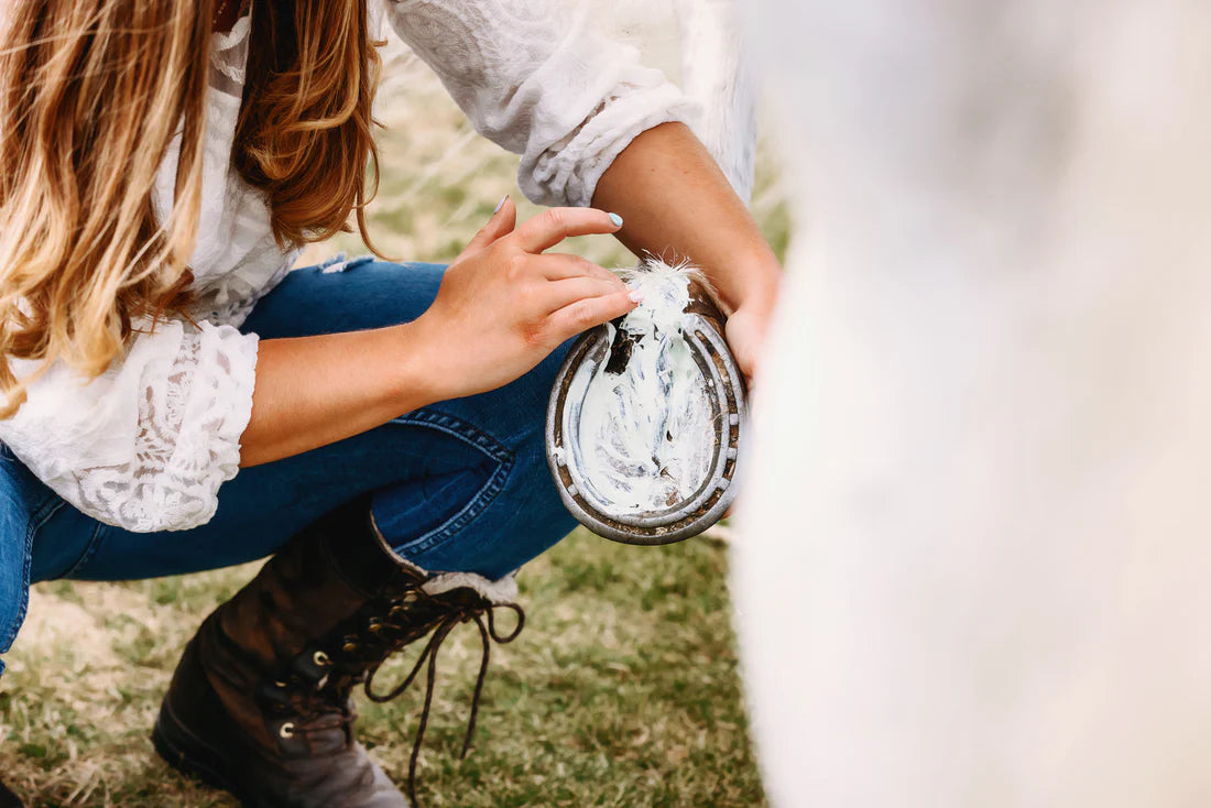 View of a woman applying Equiderma Thrush & Whiteline to the bottom of a white horse's foot