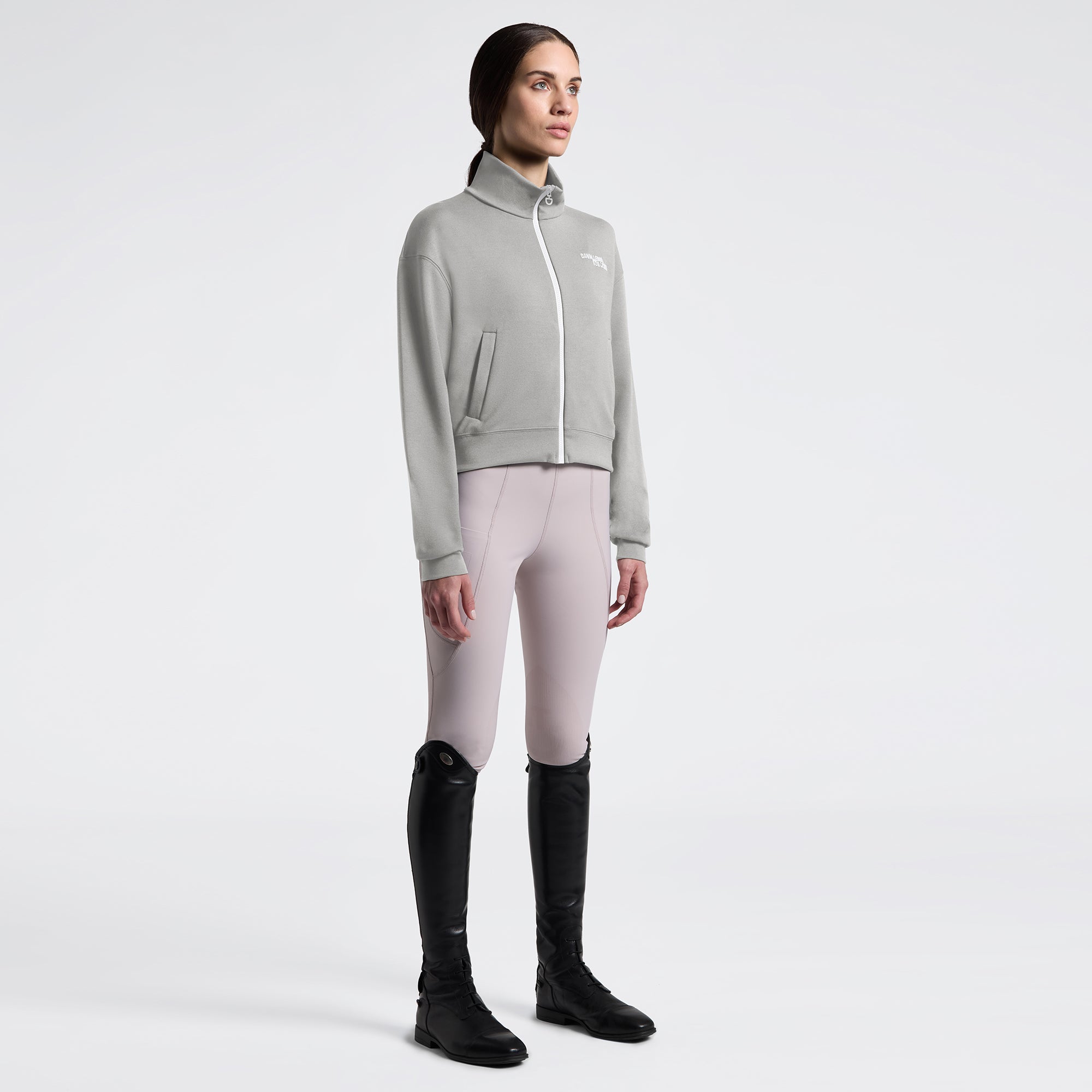 Angled front full length view a model wearing the Cavalleria Toscana Jersey Zip Sweatshirt In Belgian Block, light colored breeches, and black tall boots.