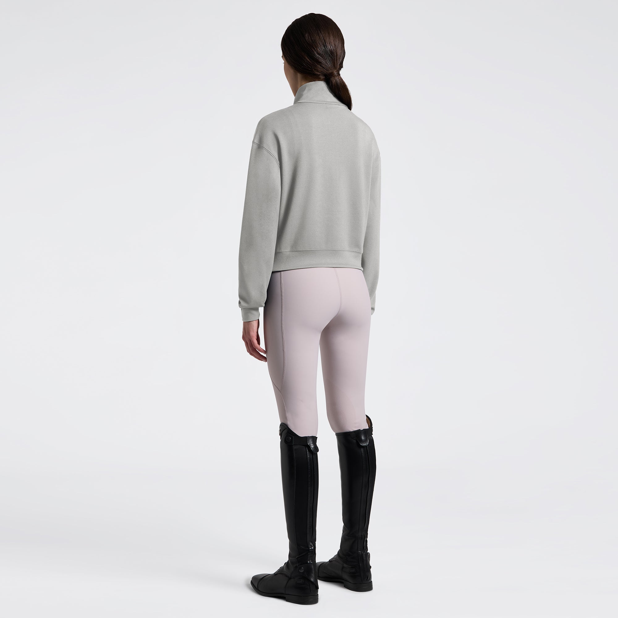 Angled back full length view a model wearing the Cavalleria Toscana Jersey Zip Sweatshirt In Belgian Block, light colored breeches, and black tall boots.