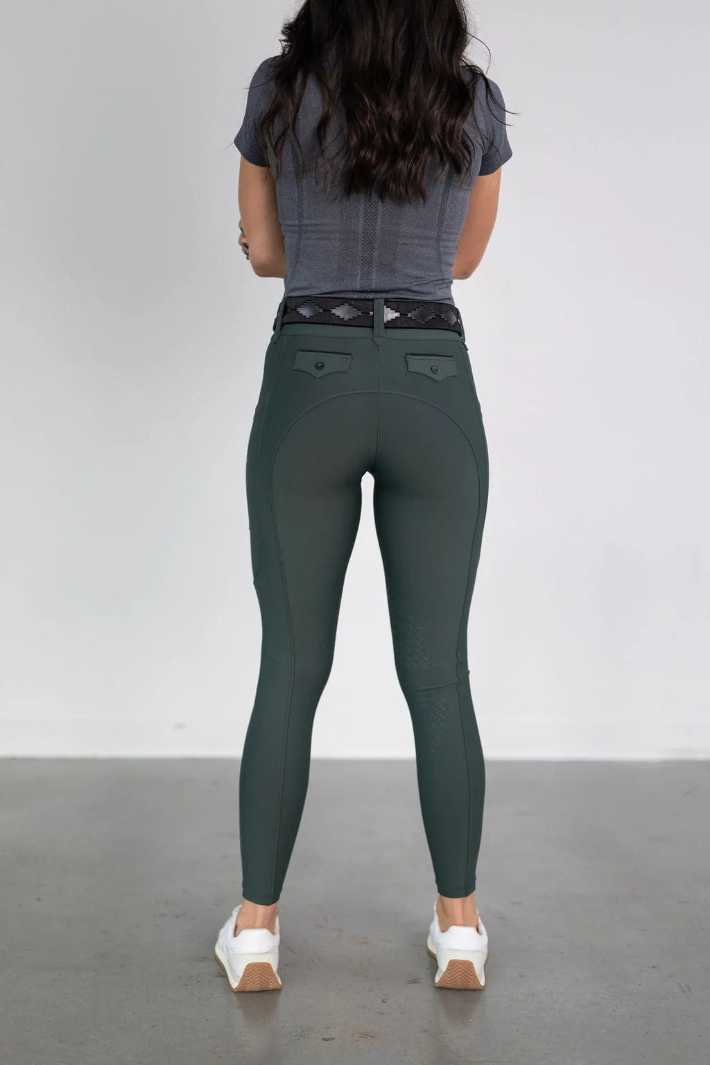 Back view of a female model wearing the green Free Ride Lux Knee Patch Breeches in a studio setting