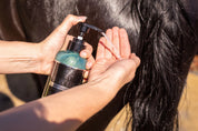 Hand dispensing Hairy Pony Silky Serum onto palm beside a horse’s dark tail