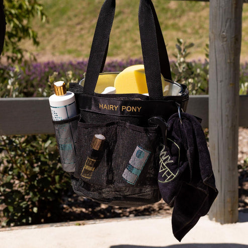 View of the Hairy Pony Horse Wash Bay Bag filled with bathing supplies and a fence in the background