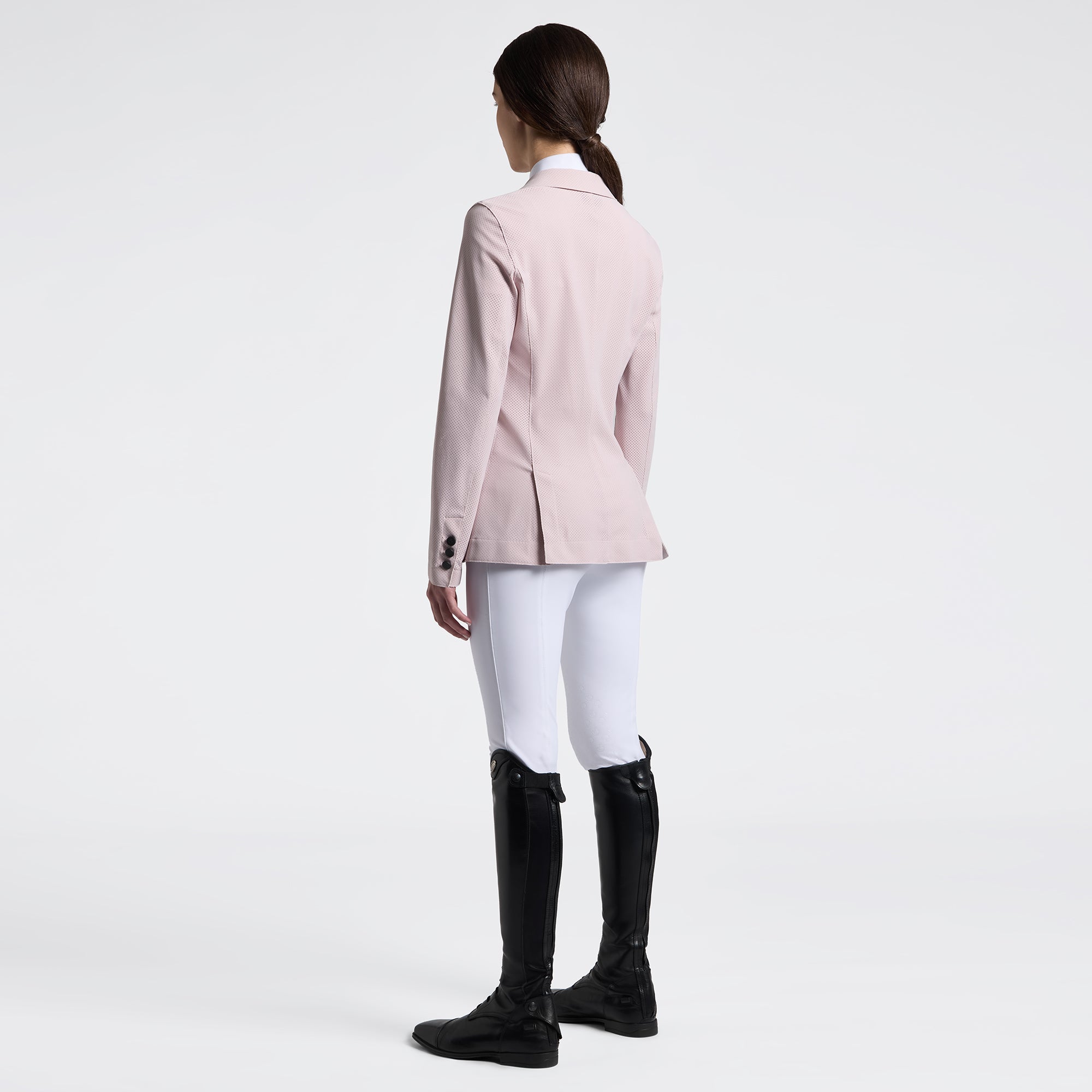 Full body angled back view of a female model wearing the pink Cavalleria Toscana Raw Cut Competition Jacket and white breeches on a plain background