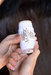 View of a model holding the Hairy Pony Plaiting Taming Wax with a dark colored horse in the background