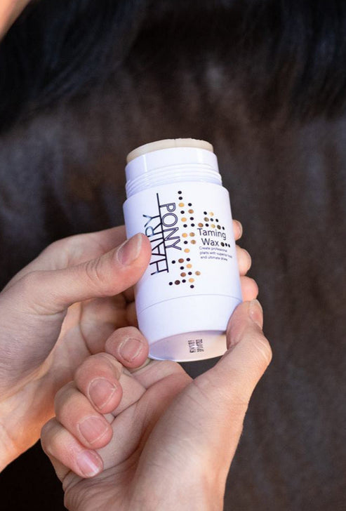 View of a model holding the Hairy Pony Plaiting Taming Wax with a dark colored horse in the background