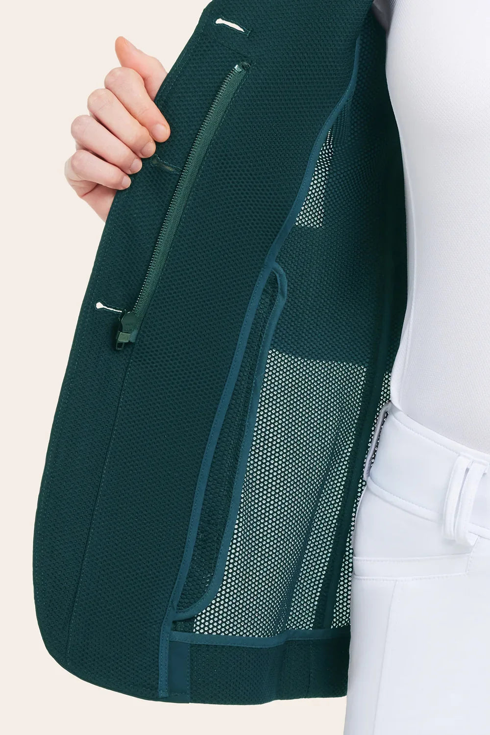 Close-up of the green mesh show coat opened to show an inside zip pocket and mesh lining, worn over a white top and white breeches.