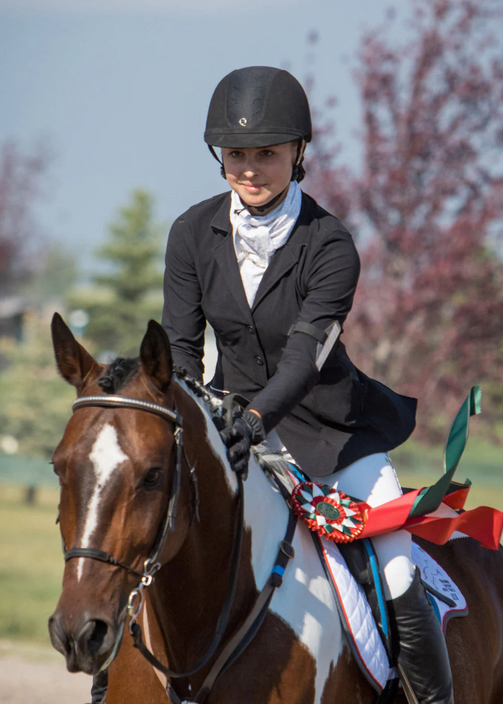 Front view of a female model wearing the black Kerrits Stretch Competitor Koat 3 Snap while riding a paint horse