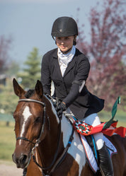 Front view of a female model wearing the black Kerrits Stretch Competitor Koat 3 Snap while riding a paint horse
