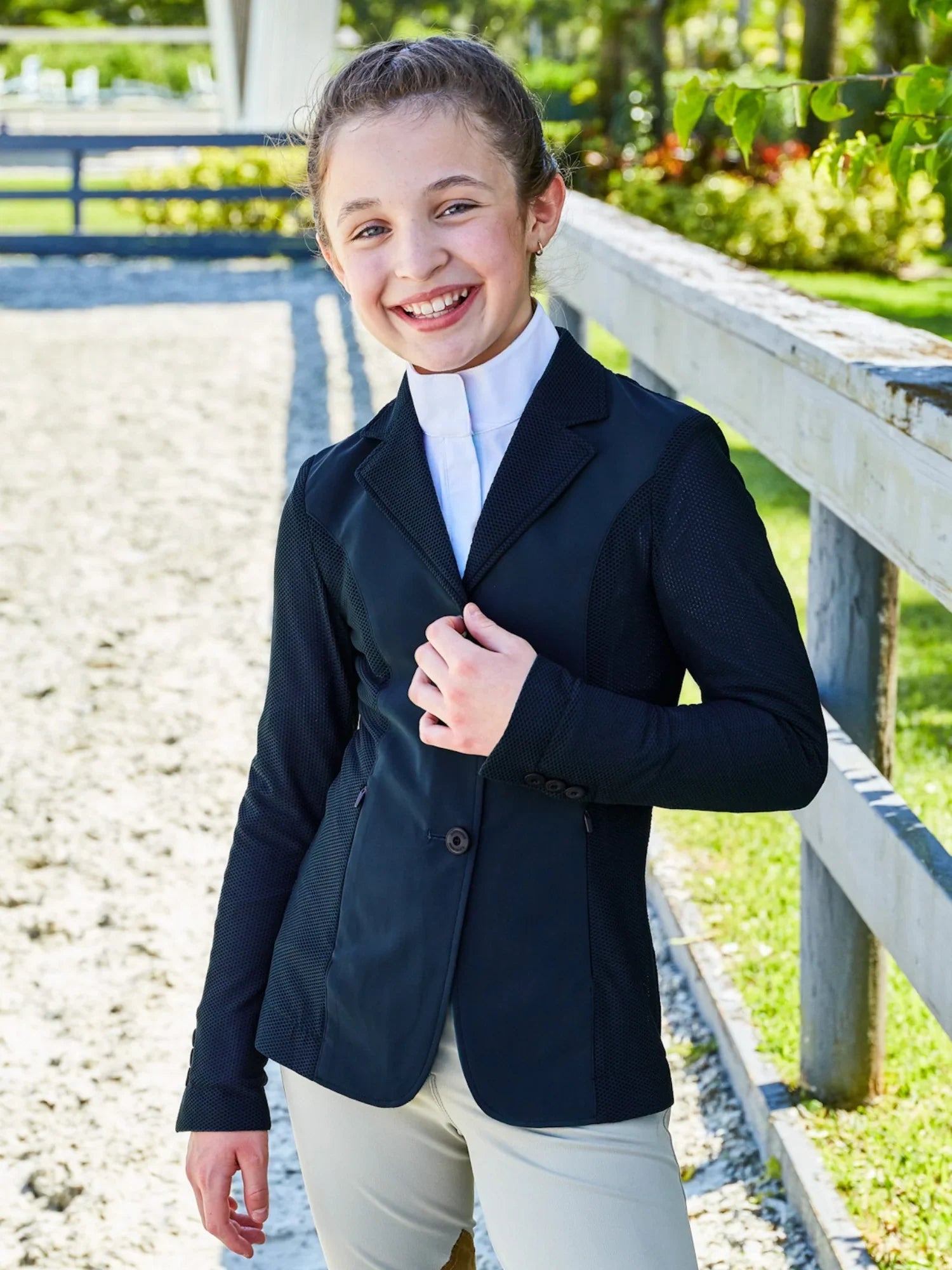 Front view of a young female model wearing the navy RJ Classics Girls' Harmony Jr. Mesh Show Coat while standing in an outdoor arena