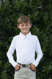 Front view of a young male model wearing the white Free Ride Equestrian Boy's Competition Shirt with green bushes in the background