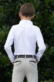 Back view of a young male model wearing the white Free Ride Equestrian Boy's Competition Shirt with green bushes in the background