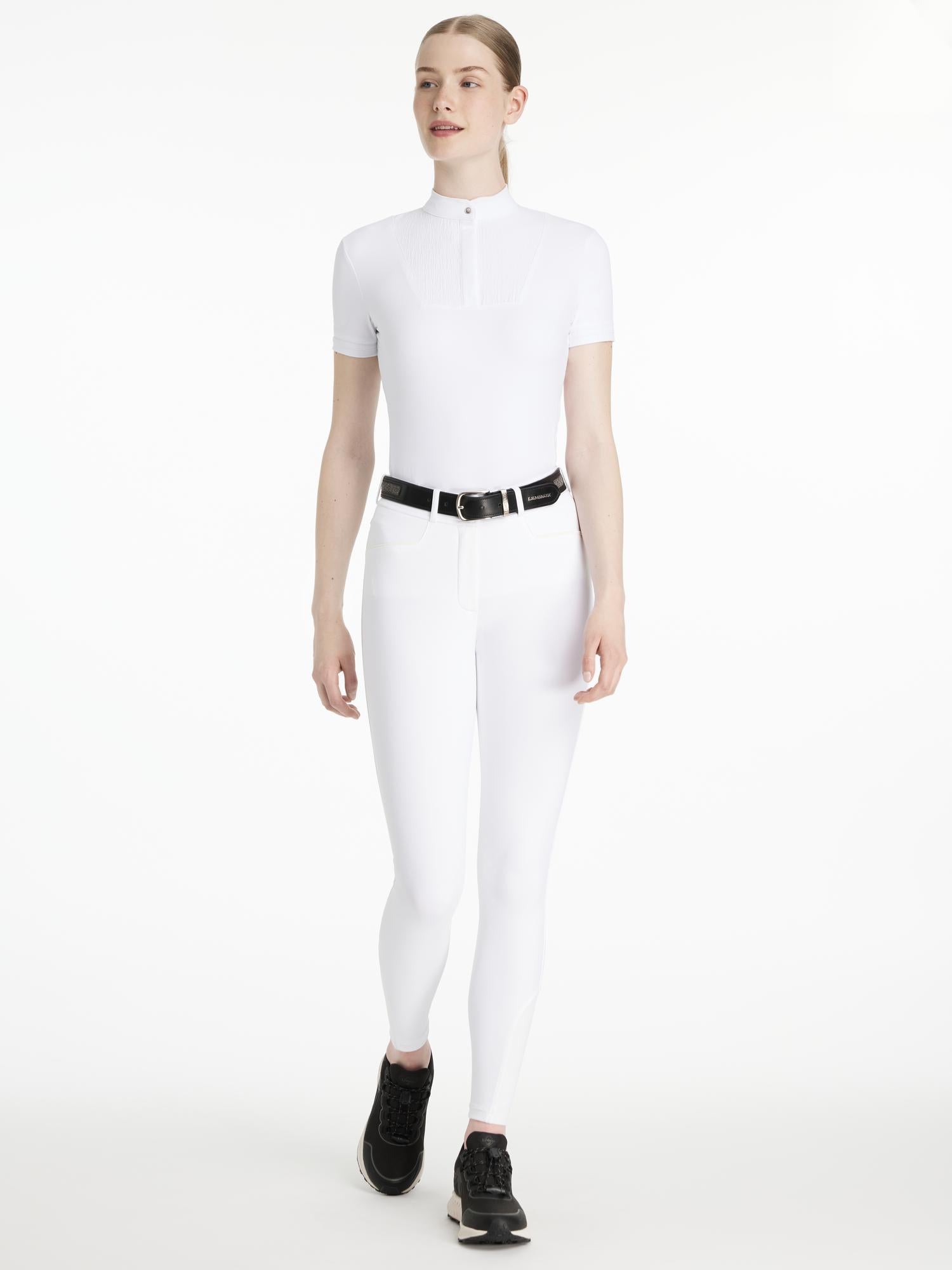 Model wearing LeMieux Isabelle Full Seat Breeches in White with black belt and black athletic shoes