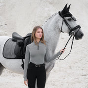 Front view of a female model wearing the gray LeMieux Aspen Herringbone Baselayer while standing in front of a gray horse with a rocky background
