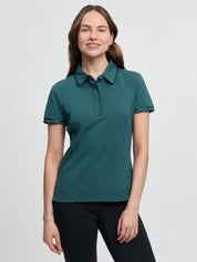 LeMieux Pixie polo shirt in jungle green with short sleeves, pointed collar, and partial button placket, shown on a model wearing black tights against a light gray background.
