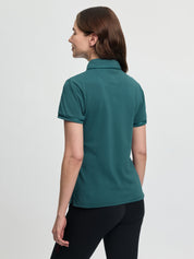 Back view of the LeMieux Pixie polo shirt in jungle green showing a pointed collar and short sleeves with piping, worn with black tights against a light gray background.