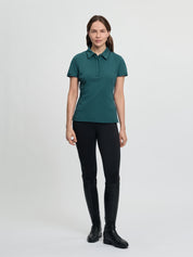 Full-body view of the LeMieux Pixie polo shirt in jungle green with a pointed collar, partial button placket, and short sleeves, worn with black tights and tall black riding boots against a light gray background.
