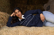 Model lying on hay wearing navy LeMieux Rochelle Rugby Shirt with white collar and chest piping detail.
