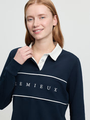 Close-up of the LeMieux Rochelle rugby shirt in navy showing the white collar with button placket, white piping across the chest, and “LEMIEUX” lettering on the front, on a model against a light gray background.