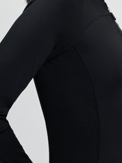 Close-up side view of the LeMieux Airflow Long Sleeve Base Layer in black showing seam panels and a perforated section along the side of the torso against a light gray background.