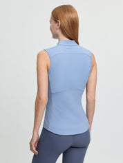Back view of the LeMieux Airflow sleeveless base layer in powder blue showing the high collar, curved seam panels, and a small perforated section at mid-back, worn with blue riding tights against a light gray background.