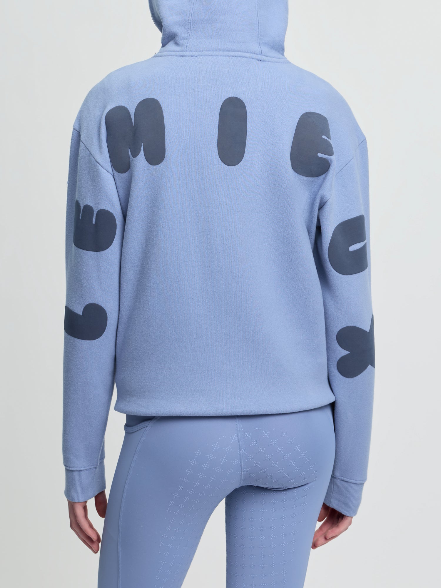 Back view of model wearing LeMieux Young Rider Sia Hoodie in powder blue with oversized LeMieux lettering on sleeves and back