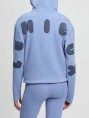 Back view of model wearing LeMieux Young Rider Sia Hoodie in powder blue with oversized LeMieux lettering on sleeves and back