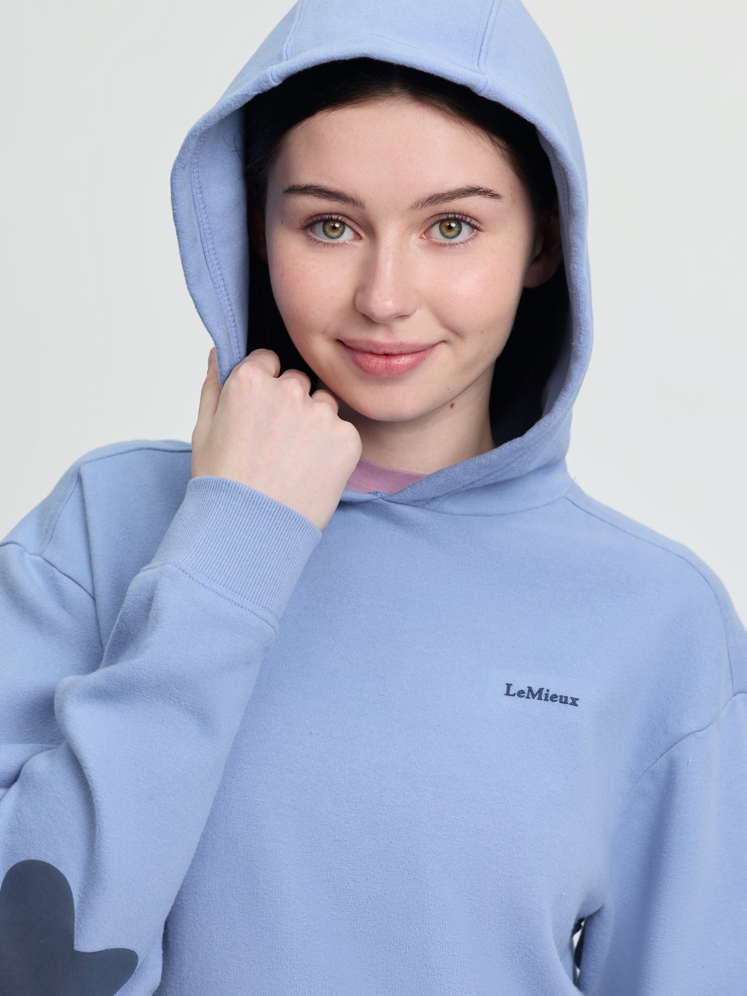Close-up of model wearing LeMieux Young Rider Sia Hoodie in powder blue with hood up and LeMieux chest logo