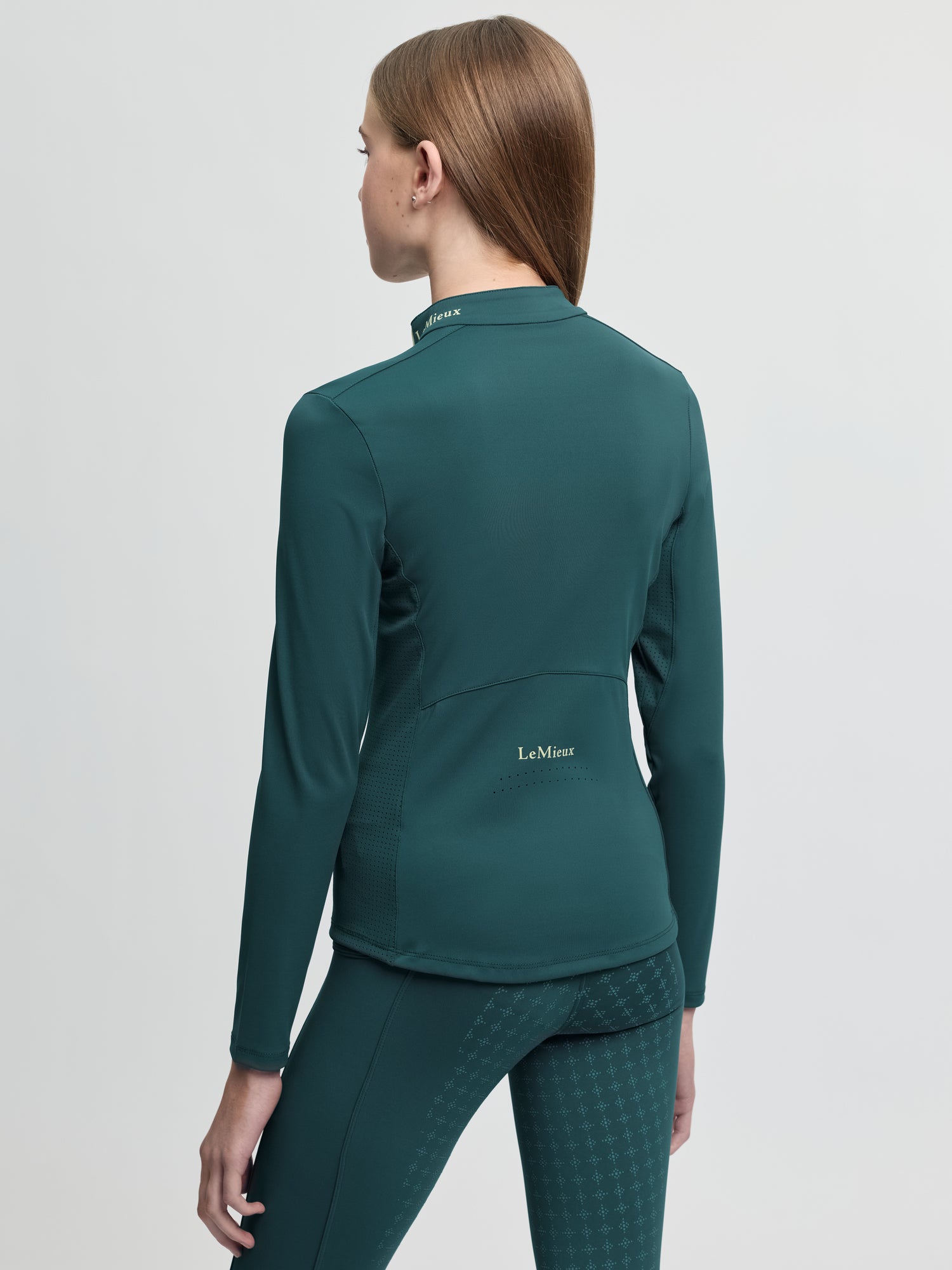 Back view of model wearing LeMieux Young Rider Airflow Base Layer in Jungle showing high collar and LeMieux logo on lower back