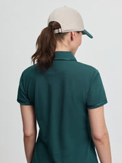 Back view of the LeMieux Pixie polo shirt in jungle green, showing the collar and short sleeves with piping, worn with a light cap with a green brim against a light gray background.