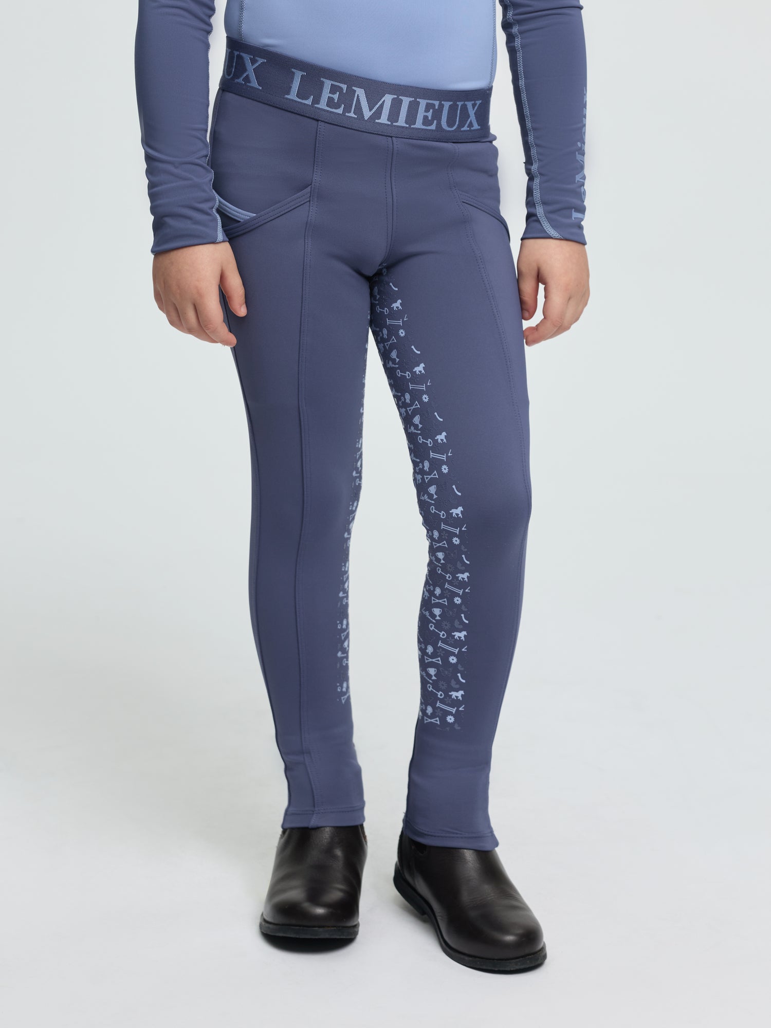 Child wearing LeMieux Mini Pull On Breech in Shadow with elastic logo waistband, side pockets, and silicone grip print on inner legs
