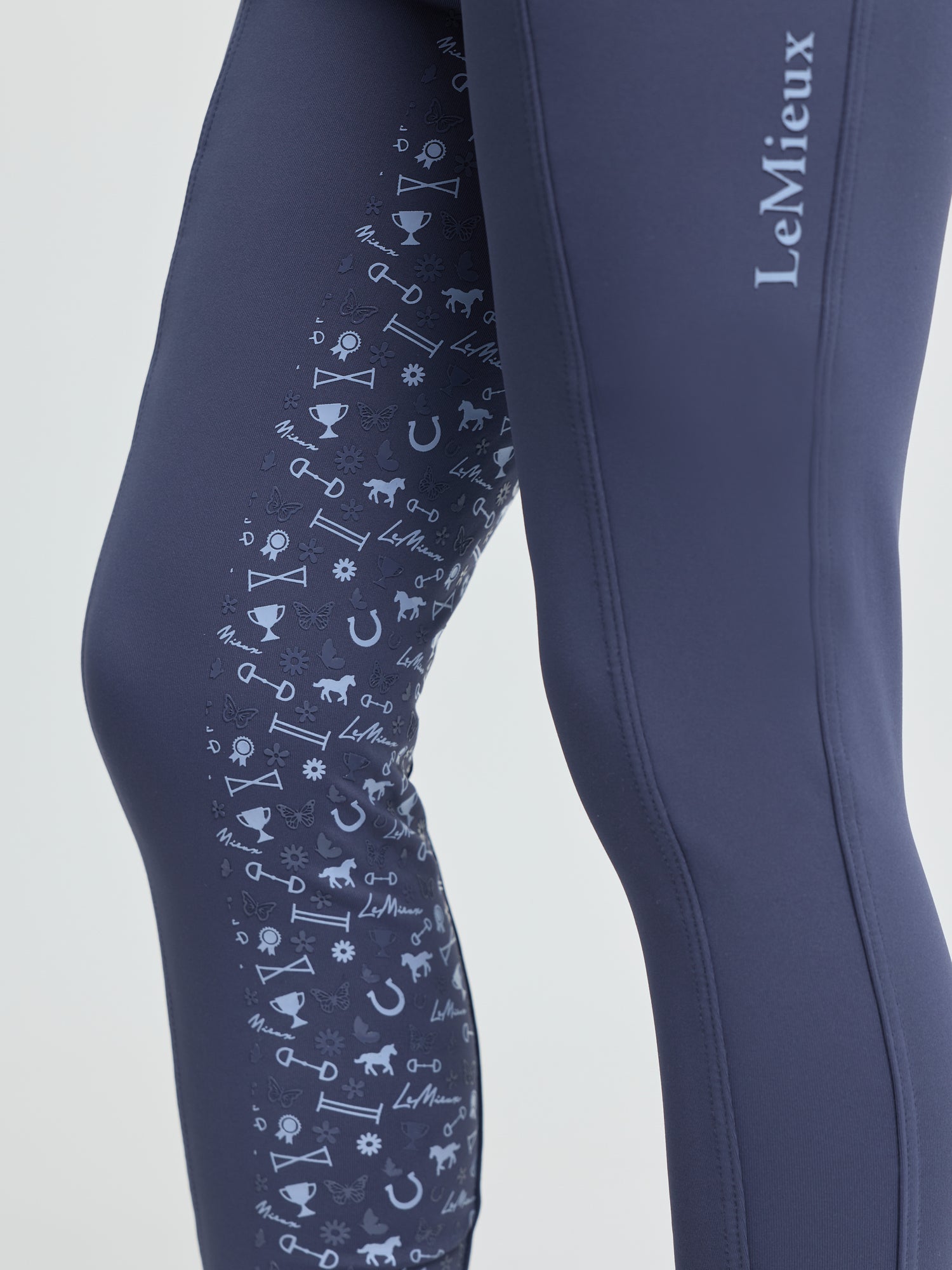 Close-up of LeMieux Mini Pull On Breech in Shadow with silicone knee grip print featuring equestrian icons