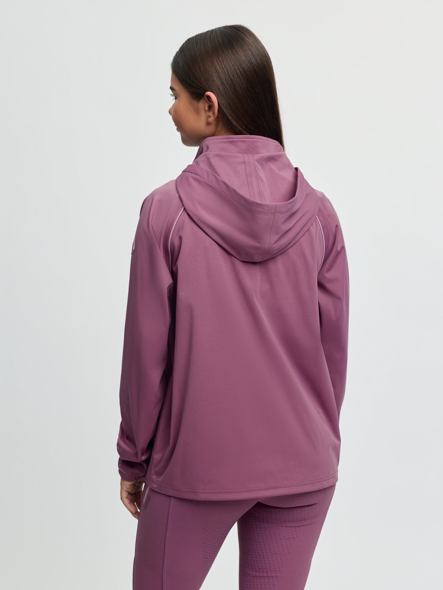 Back view of model wearing LeMieux Young Rider Paige Quarter Zip Waterproof Jacket in Mallow showing attached hood