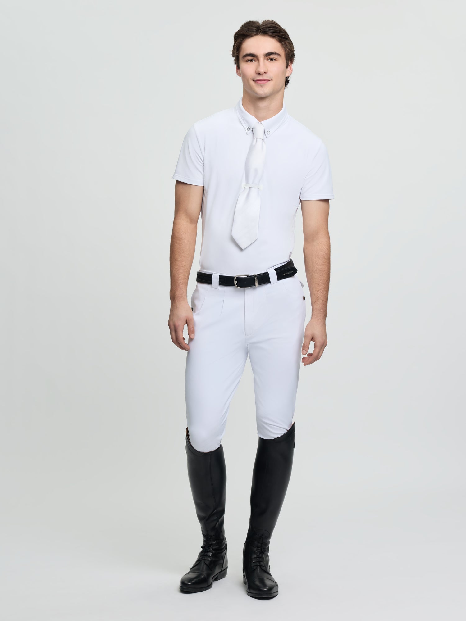 Model wearing LeMieux men’s short sleeve competition shirt in white, styled with stock tie, white breeches, and tall boots