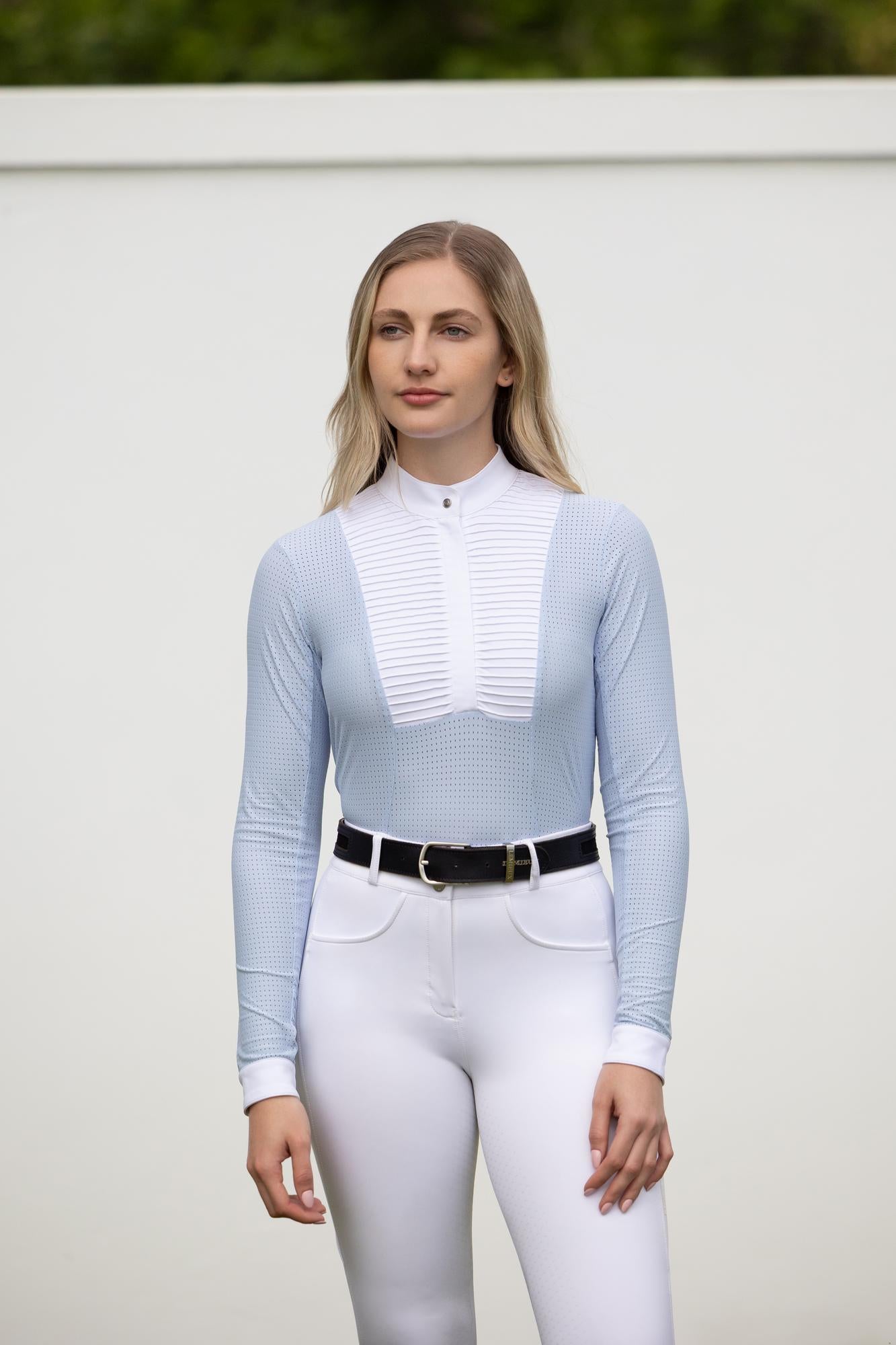 Model wearing LeMieux Arielle Long Sleeve Show Shirt in Mist with white stand collar and pleated bib front, paired with white breeches and black belt