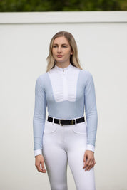Model wearing LeMieux Arielle Long Sleeve Show Shirt in Mist with white stand collar and pleated bib front, paired with white breeches and black belt