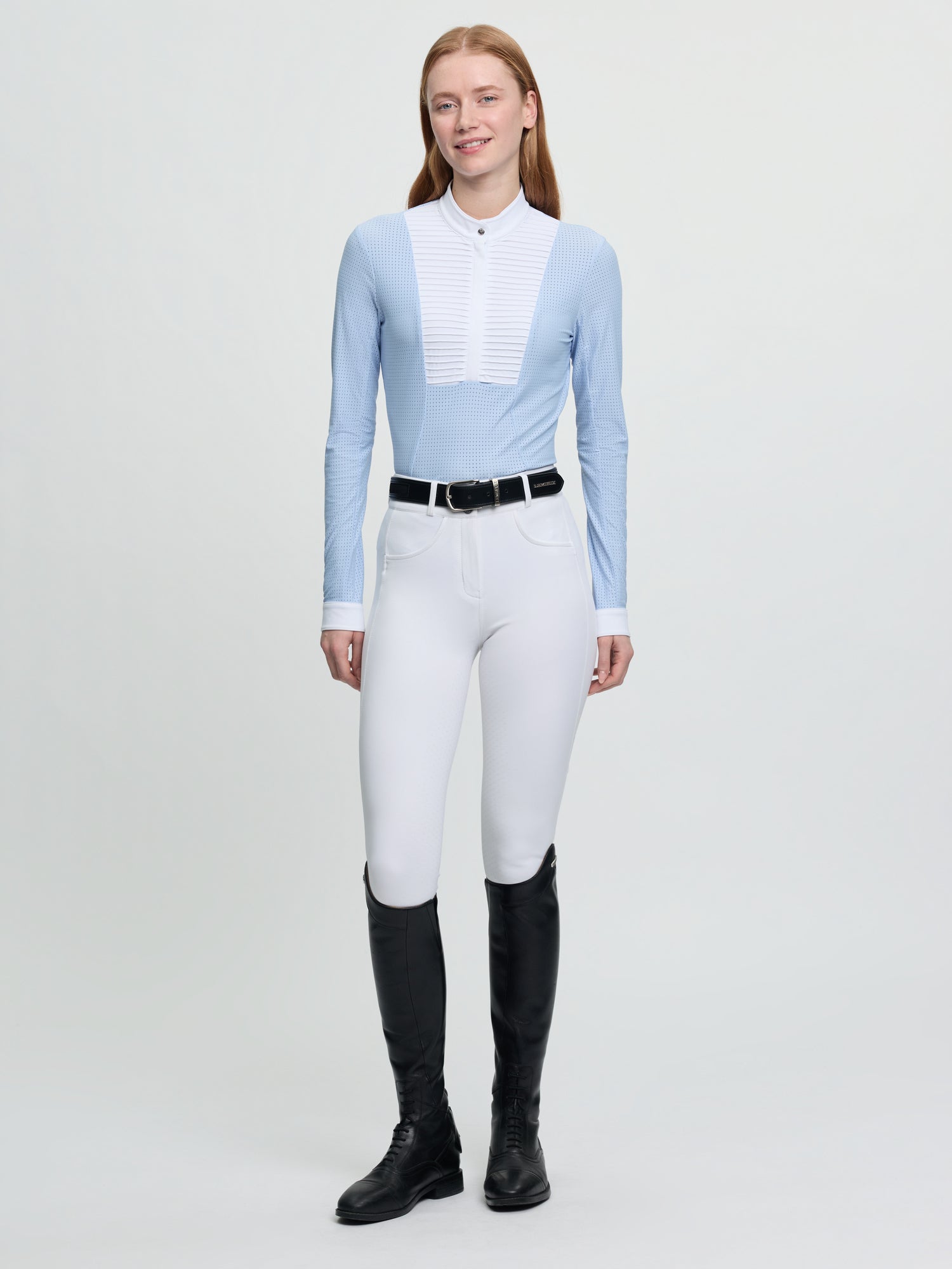 Model wearing LeMieux Arielle Long Sleeve Show Shirt in Mist with white stand collar and pleated bib front, paired with white breeches and tall boots
