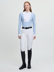 Model wearing LeMieux Arielle Long Sleeve Show Shirt in Mist with white stand collar and pleated bib front, paired with white breeches and tall boots