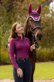 Front view of a female model wearing the Blackberry LeMieux Classique Base Layer while standing next to a horse outside
