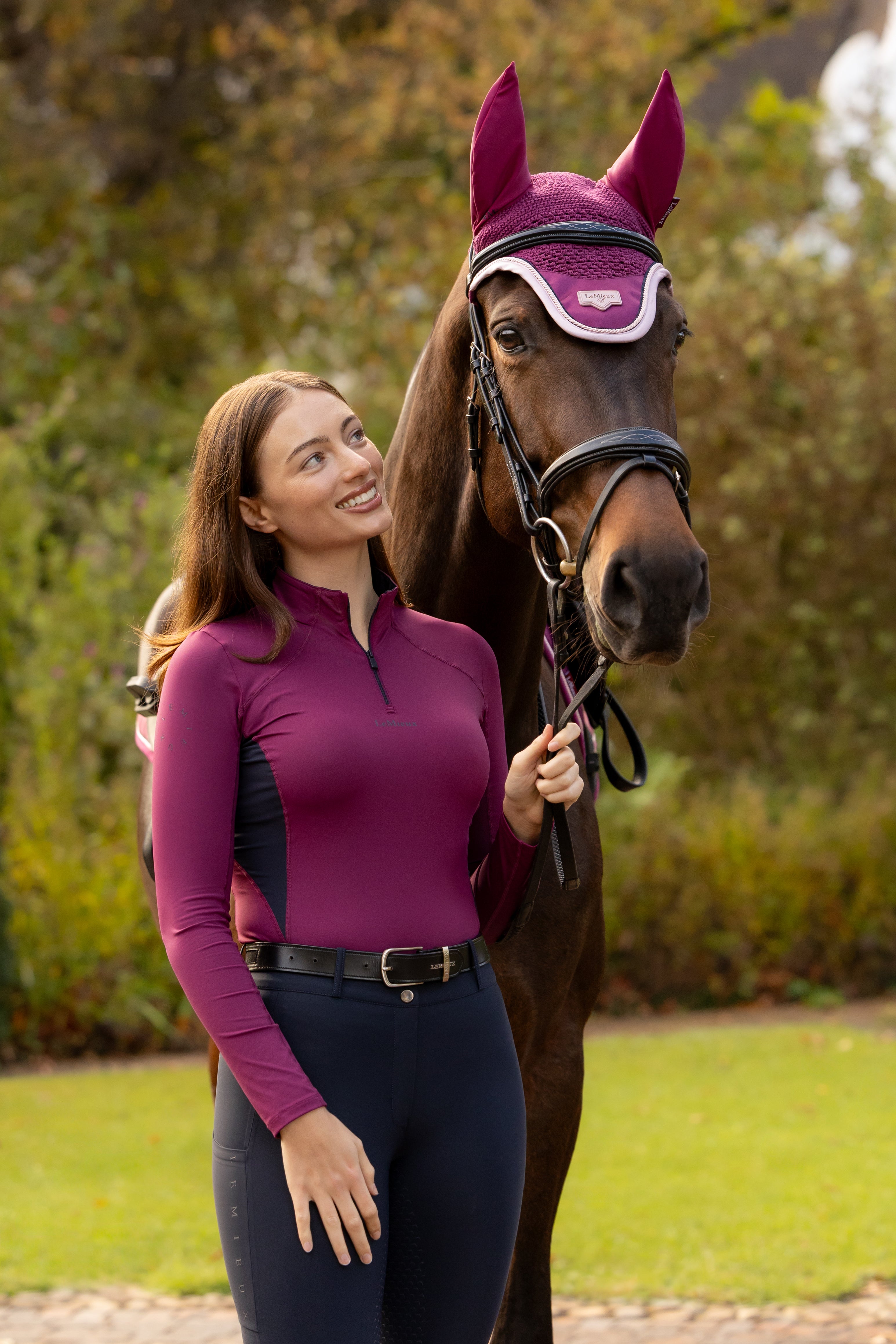Front view of a female model wearing the Blackberry LeMieux Classique Base Layer while standing next to a horse outside