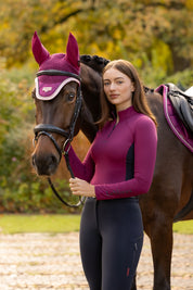 Angled front view of a female model wearing the Blackberry LeMieux Classique Base Layer while standing next to a horse outside
