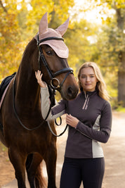 Front view of a female model wearing the Cocoa LeMieux Matilda Mid Layer while standing next to a horse outside