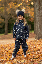 Side view of a young female model wearing Navy LeMieux Mini Pippin Splash Dungarees and standing outdoors