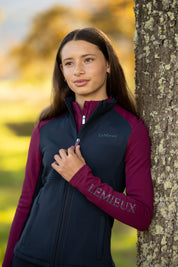Front view of a model wearing Blackberry LeMieux Young Rider Bethany Fleece Zip Through while leaning against a tree