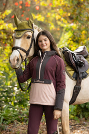 Front view of a young female model wearing Bramble LeMieux Young Rider Bailey Waterproof Anorak next to a horse outdoors