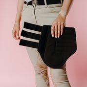 Front view of a model holding a black Ecogold Breathable Exercise Horse Boot on a pink background