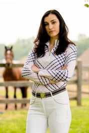 Front view of a female model wearing the white KL Select Gabrielle Breech with a horse standing in the background